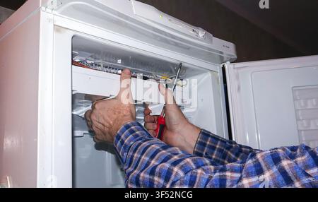 A person is actively repairing a refrigerator in a residential kitchen, using tools to fix internal components while ensuring everything is properly a Stock Photo