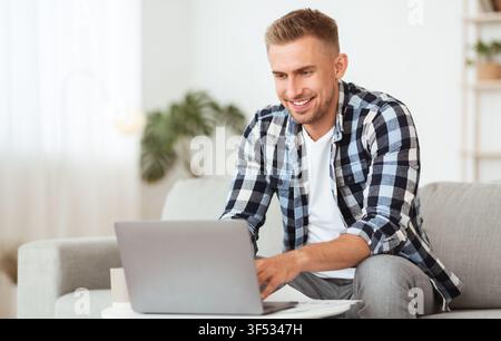Happy man using laptop sitting on couch Stock Photo