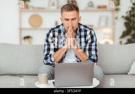 Pensive young man sitting at table, using computer Stock Photo
