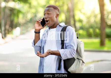 Surprised black guy having conversation on mobile phone at park Stock Photo