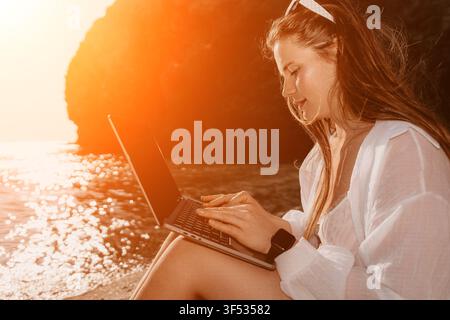 Laptop freelancer beach young woman working remotely on her computer outdoors at sunset during vacation for digital nomad lifestyle Stock Photo
