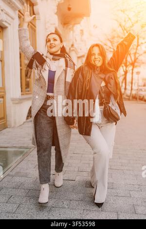 Women friends walking two joyful young women walk down a bright urban sidewalk during sunset while expressing happiness Stock Photo