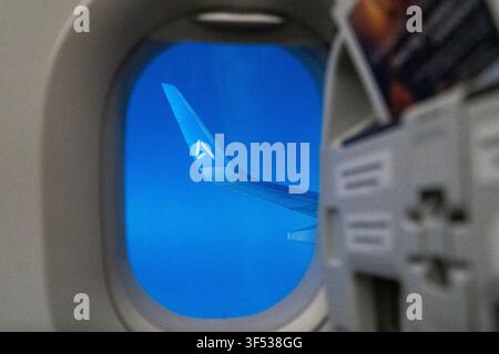 A view from an airplane window shows the wing and tail of another aircraft against a bright blue sky. Stock Photo