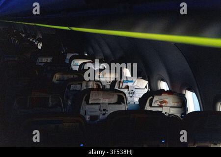 A dark airplane cabin interior with rows of empty seats illuminated by overhead lights. Stock Photo