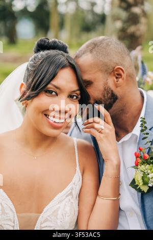 Happy bride smiling as groom whispers in her ear Stock Photo