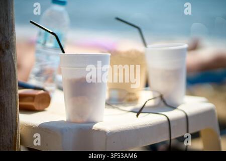 Close-up of refreshing iced coffee drinks served in white plastic cups with black straws placed on a small plastic table with a water bottle and sungl Stock Photo