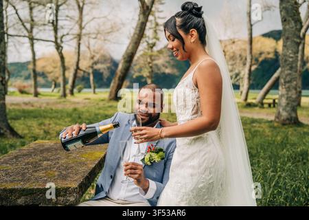 Happy newlywed couple pours champagne in a park Stock Photo