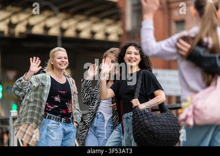 Young diverse friends smiling and waving on a city street Stock Photo