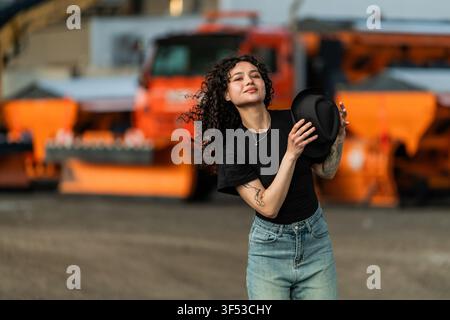 Woman holding a hat poses in front of orange trucks Stock Photo