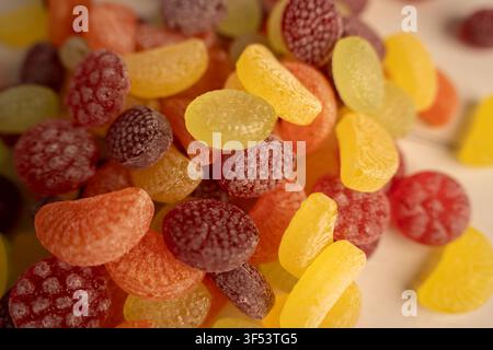 macro closeup of colorful sugar-coated gumdrops and jelly candies piled in warm light, vivid yellow orange red purple tones, frosted sugary texture, s Stock Photo