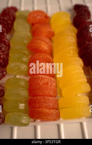 macro close-up of neatly arranged colorful sugar-coated gumdrops in vertical rows on a white plastic tray, showcasing translucent glossy textures, war Stock Photo