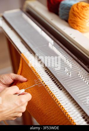 Knitting machine producing orange knitted fabric. Textile crafting process with yarn and knitting equipment. Stock Photo