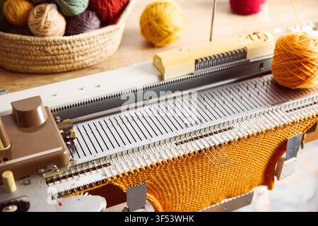 Knitting machine producing orange knitted fabric. Textile crafting process with yarn and knitting equipment. Stock Photo