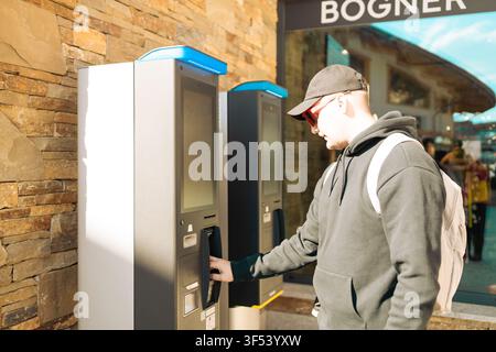 Young man using outdoor automated self-service machine in modern resort town Stock Photo