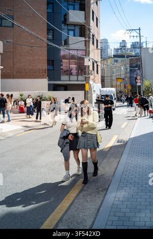 Two young women walking down a sunny street in Seongsu-dong, Seoul, looking at a smartphone together. Stock Photo