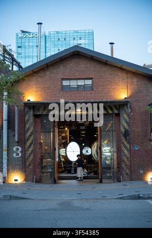 Exterior facade of a red brick industrial-style building with a large illuminated entrance in Seongsu-dong, Seoul, at dusk. Stock Photo