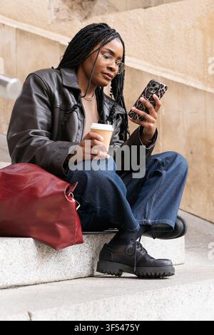 Young student using smartphone and drinking coffee on university steps Stock Photo