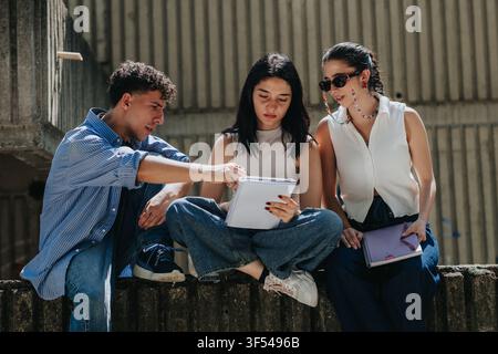 Three students studying together outdoors on campus reviewing notes and discussing coursework Stock Photo