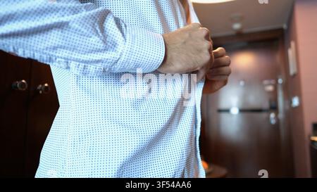 Close up of male hands of young businessman buttoning shirt cuffs in modern hotel room or apartment interior. Confident entrepreneur preparing formal Stock Photo