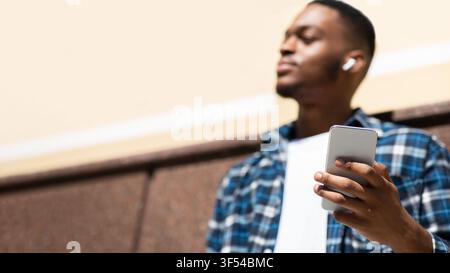 Portrait of man listening to music leaning against wall Stock Photo
