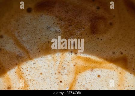 Macro view of freshly brewed coffee showing textured crema, tiny air bubbles, and swirling patterns of brown foam on the surface of a hot beverage. Stock Photo