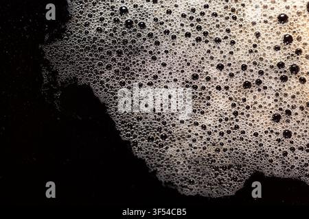 Close-up macro shot of rich dark coffee crema featuring a dense layer of small bubbles and froth forming abstract patterns across the surface. Stock Photo