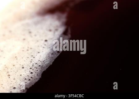 Close-up view of rich dark coffee crema and tiny bubbles floating on the surface of a fresh hot beverage, showing smooth liquid texture. Stock Photo