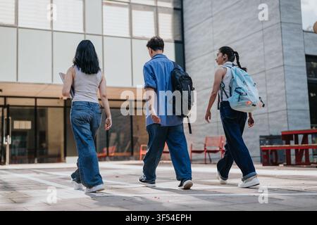 Three students walking on campus courtyard with backpacks and casual clothing Stock Photo