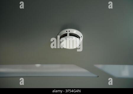 White smoke detector mounted on a gray ceiling, representing fire safety and home monitoring systems for emergency detection and hazard prevention Stock Photo