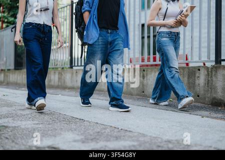Three students walking on campus wearing casual jeans and carrying books and backpacks Stock Photo