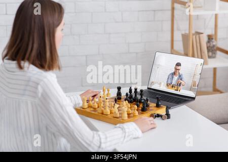 Online chess at home. Girl and guy play on board games using laptop Stock Photo