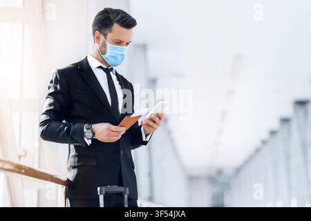 Entrepreneur in face mask using phone while waiting for flight Stock Photo