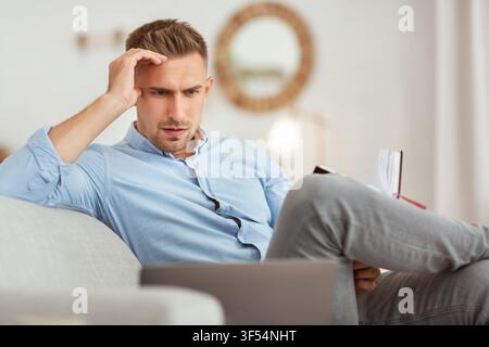 Portrait of pensive man sitting on couch using pc Stock Photo