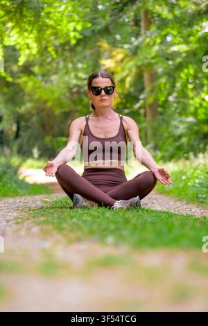 fit woman sitting meditating and practicing yoga in a forest Stock Photo