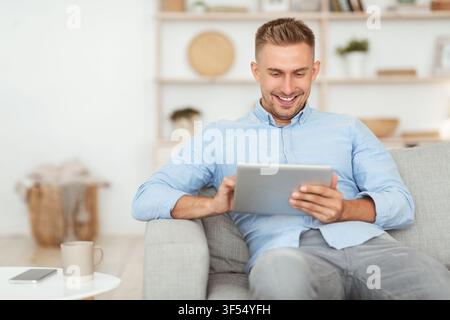 Happy man using digital tablet sitting on sofa Stock Photo