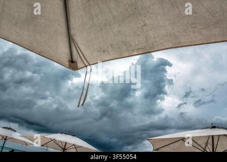 White beach umbrellas set against a dramatic, stormy sky. Stock Photo