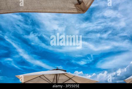 large beach umbrellas against a cloudy blue sky Stock Photo