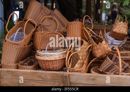 A variety of woven wicker and straw baskets in different shapes and sizes displayed on a rustic wooden shelf in an outdoor market setting. Stock Photo