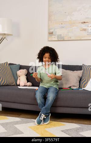 Curly-haired african american boy engages in fun indoor activities while sitting on the couch Stock Photo