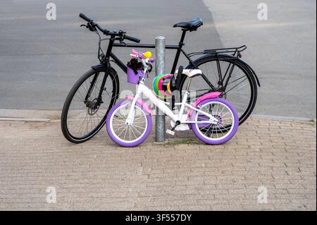 Adult black city bicycle and small colorful children bike parked together on street. Family city bicycle trips Stock Photo