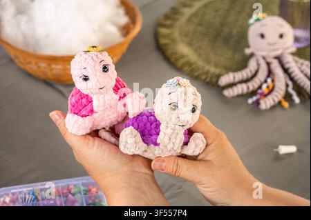 Close up of woman hands holding two finished plush turtle toys. Demonstrating handmade cute amigurumi animals. Cozy home crochet hobby Stock Photo