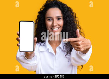 Mockup Image Of Brunette Woman Pointing At Smartphone With Blank White Screen Stock Photo