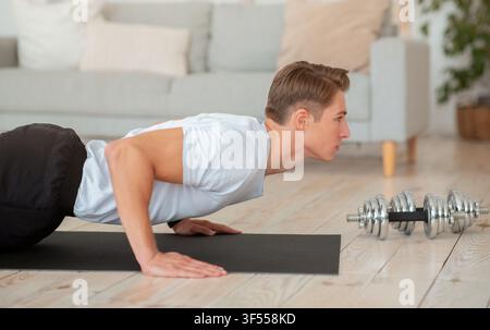Morning workout. Handsome guy doing push-ups on mat in living room Stock Photo