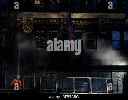 A lone construction worker in bright safety gear stands on a scaffold below the United States flag on a historic NYC building Stock Photo