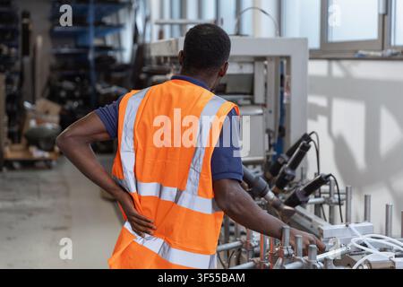 A factory worker is operating machines on a production line. He is suffering from lower back pain. Stock Photo