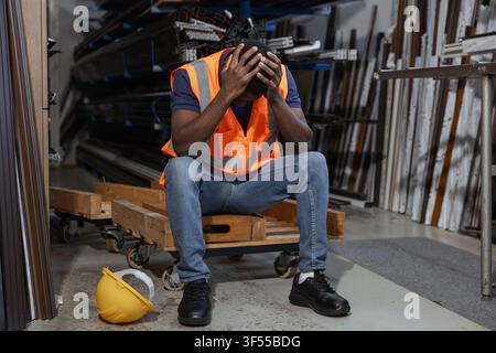 Burnout worker sits on a pallet in an industrial space, holding his head in his hands after a tiring day. Stock Photo