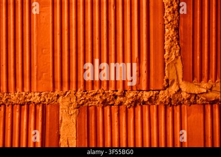 Close-up view of a newly constructed wall made of large red porous ceramic blocks, bonded together with mounting foam mortar in a construction setting. Stock Photo