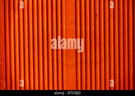 Close-up abstract background of a vibrant orange ceramic wall featuring vertical parallel ridges and a modern architectural pattern. Stock Photo