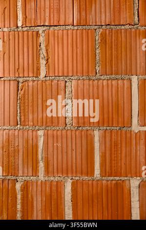 Close-up vertical background view of a newly built masonry wall constructed with red porous ceramic blocks and mortar joints on a construction site. Stock Photo