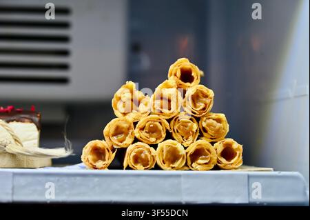 Close-up view of a pyramid stack of sweet, crispy golden waffle rolls filled with boiled condensed milk, displayed on a shelf in a pastry shop or cafe display case. Stock Photo